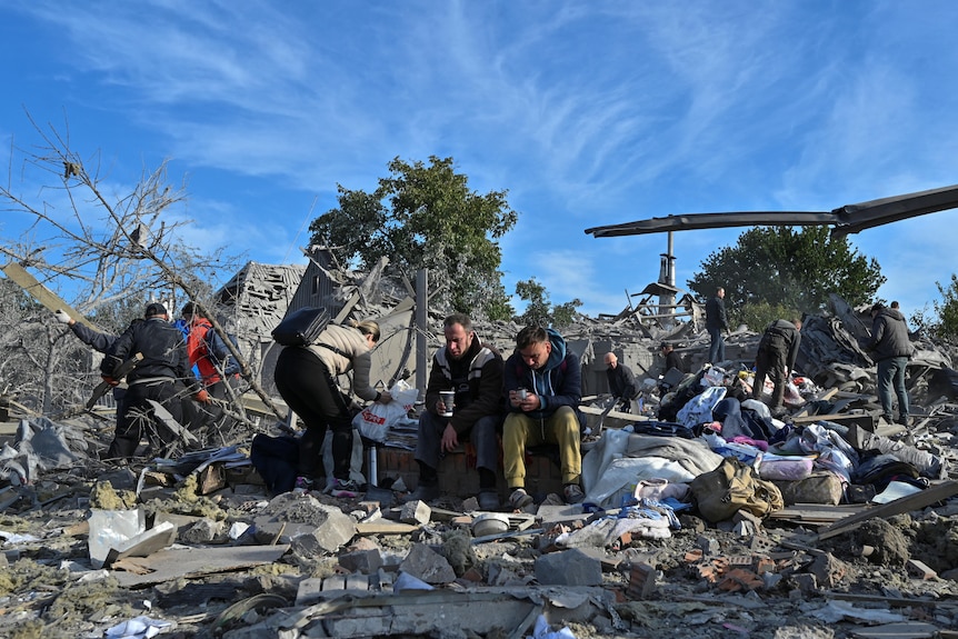 Distressed local residents sit at a site of a residential area heavily damaged by a Russian missile strike
