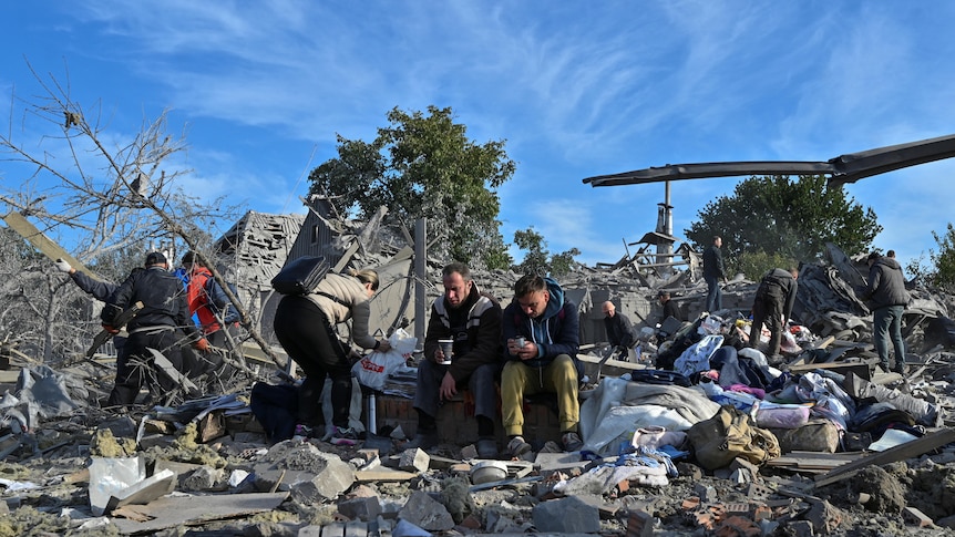 Distressed local residents sit at a site of a residential area heavily damaged by a Russian missile strike