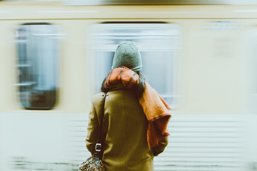 The back of a woman standing in front of a moving blurry train