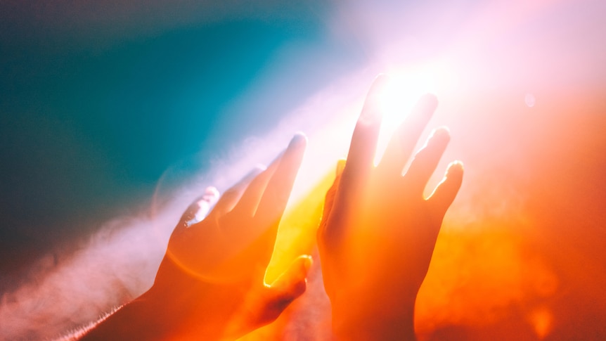 Image of someone's hands up in the air, open towards a stream of rainbow light.