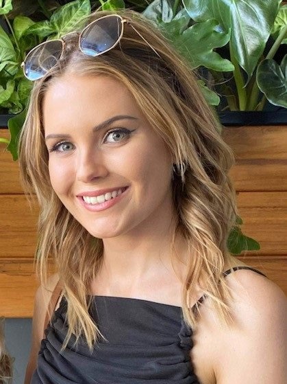 A young girl from the shoulders up in a black dress and with sunglasses on her head. 