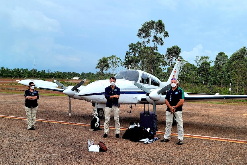 Four people socially distance by a small plane.