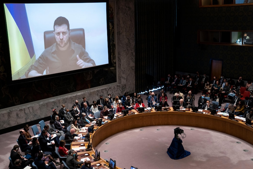 The UN security council sits in a circle, watching Zelenkyy's speech from a screen.