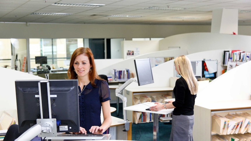 Two women in an office, both using a standing desk and working on their computers