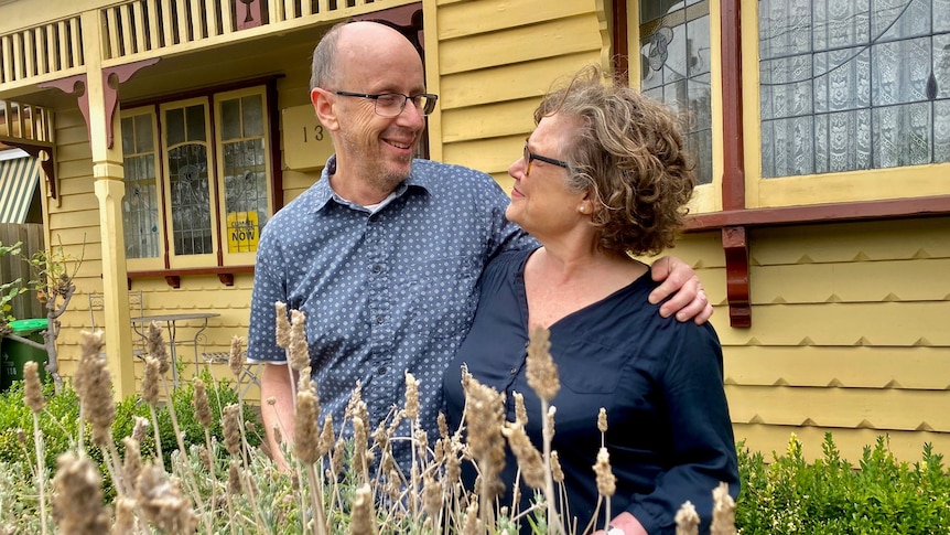 A heterosexual couple in their fifties embrace in their front garden 