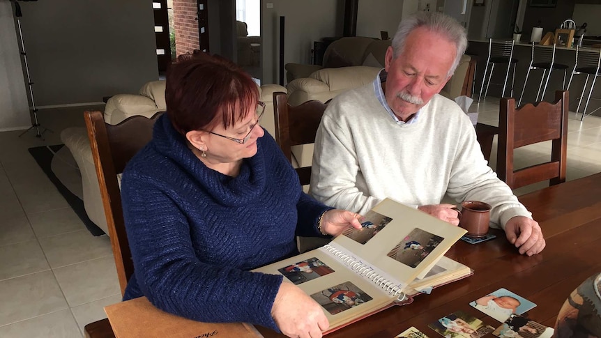 A man and woman sit at a table looking through a photo album.
