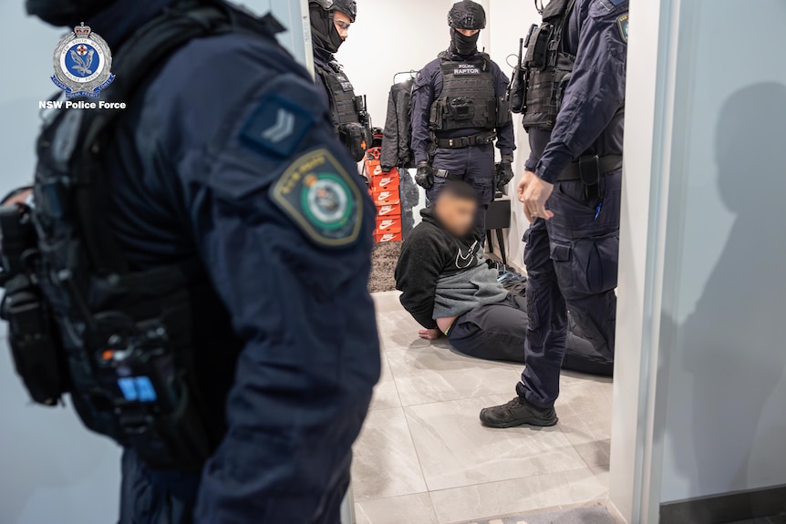 new south wales police as part of taskforce magnus arrest a man who is sitting down on the ground with handcuffs