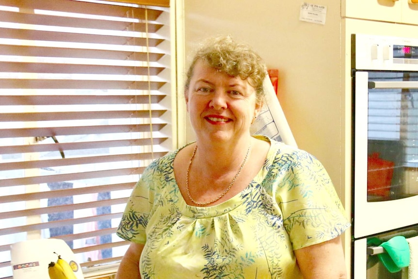 Jackie Creighan in a yellow dress standing in his kitchen