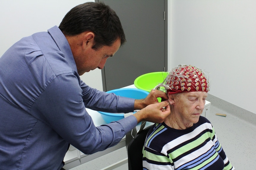 Man removes cap with electrodes and wires from a woman's head.