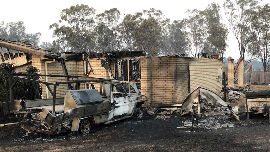A ute and tinny have been melted away next to a brick house that was destroyed by fire.