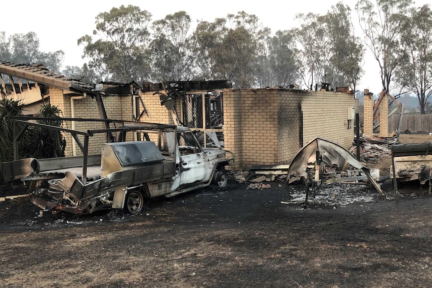 A ute and tinny have been melted away next to a brick house that was destroyed by fire.