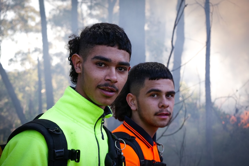 Portrait of two young men with smoke and gentle fire in the background.