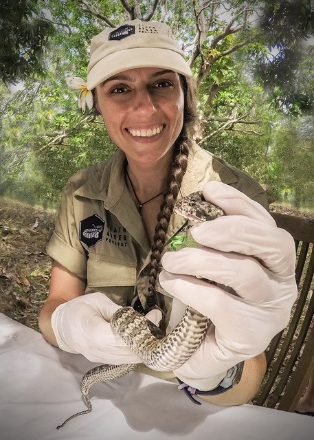 A woman smiling and holding the mouth a snake with rubber gloves on