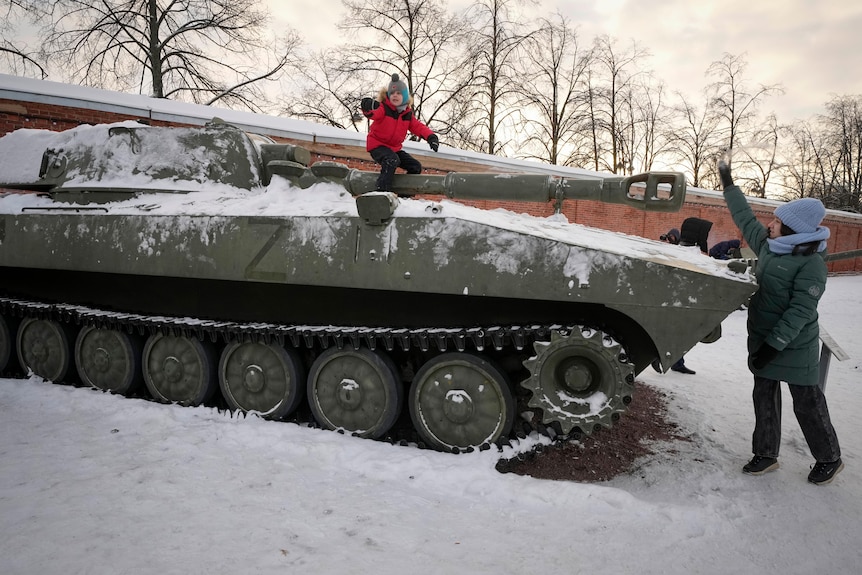 A young boy plays atop a military tank in the snow. 