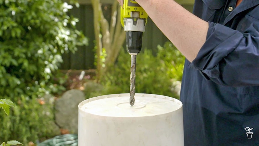 A hole being drilled in the base of an upturned white bucket.