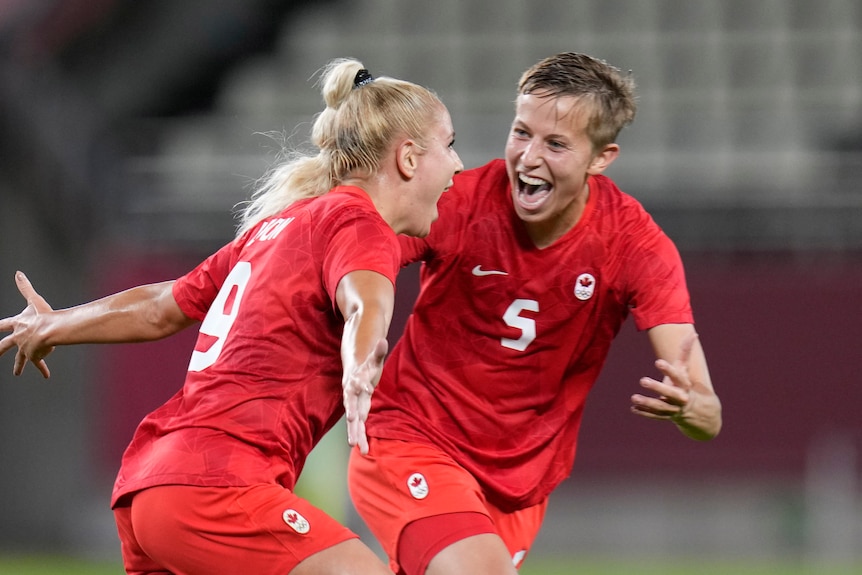 Two people in red shirts celebrate after scoring a goal in football. 