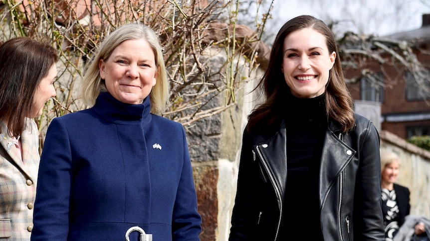 A blonde woman in blue coat next to a woman with brown hair and black leather jacket