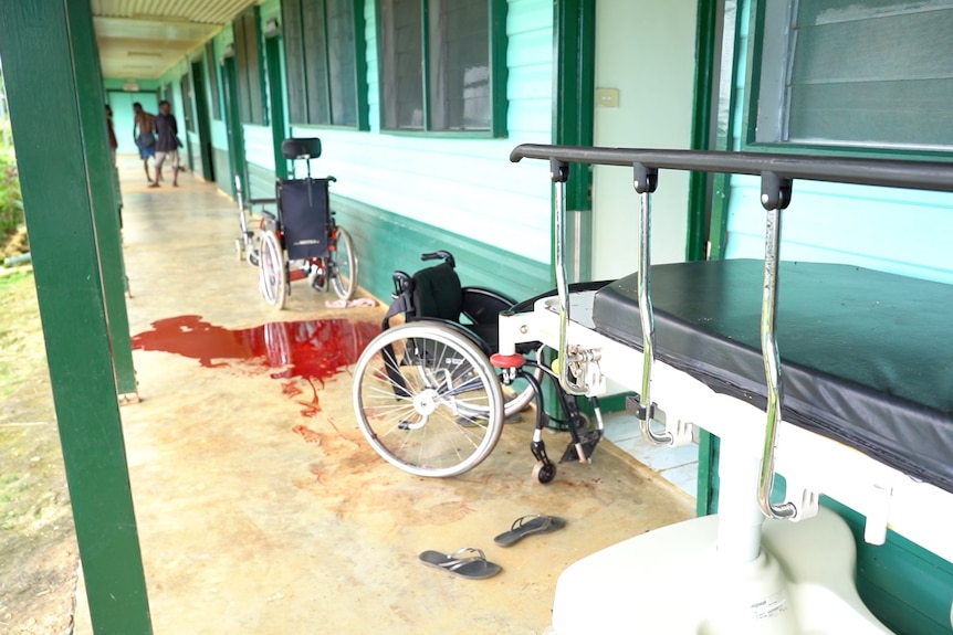 A pool of red blood on the ground next to a wheelchair and discarded pair of thongs