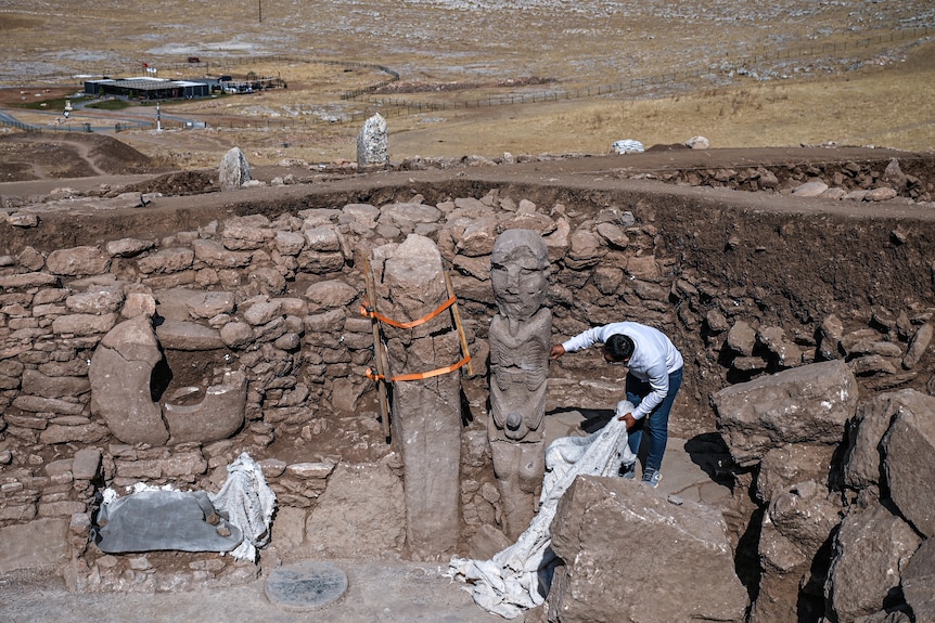 An archaeology site with a worker inspecting the human statue.