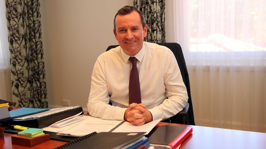 WA Premier Mark McGowan seated behind his desk in his office, hands clasped in front of him.
