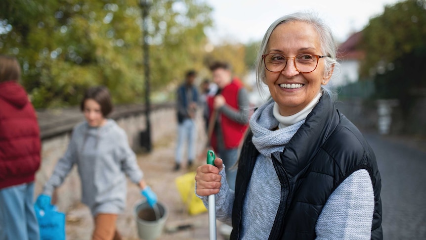 An older woman holds a broom, helping clean up an outdoor space.