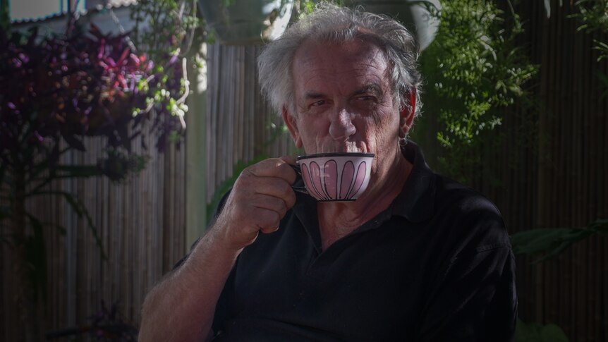 A man drinking a sip of tea from a white teacup.
