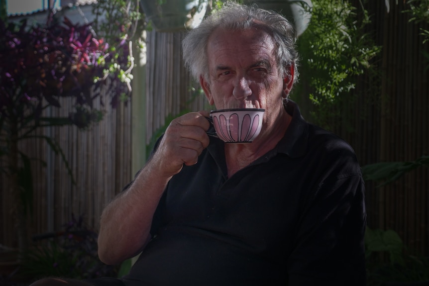 A man drinking a sip of tea from a white teacup.