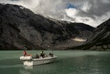 tourists travel in a small boat towards the Nigardsbreen glacier in Jostedal, Norway