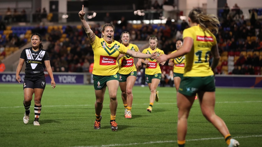 An Australian women's rugby league player roars and points her finger in the air as her teammates runs back after a try.