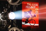 A film projector shines light through the book cover of The Rosie Project.