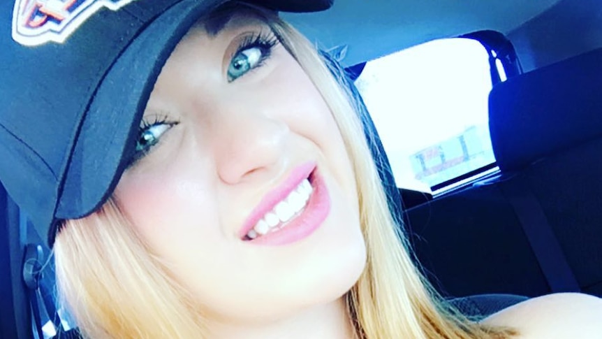 A woman wearing a hat and black singlet top takes a selfie while sitting in a car.