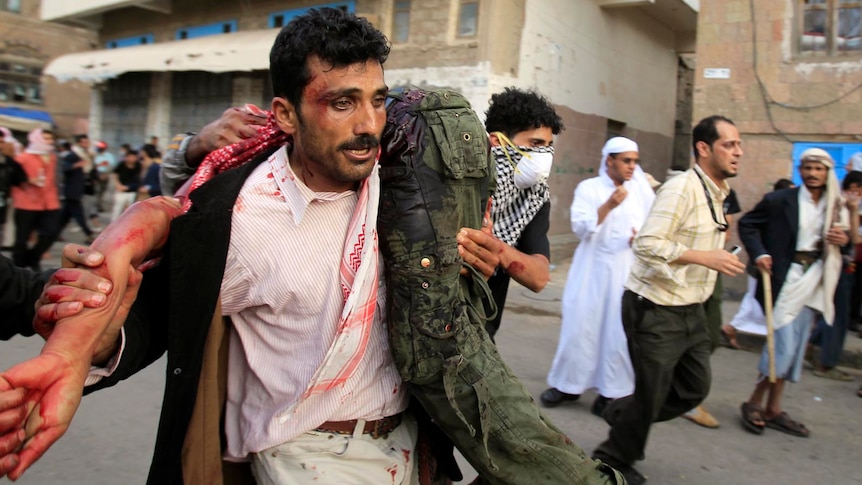 An anti-government protester carries an injured protester over his shoulder during clashes in Sanaa