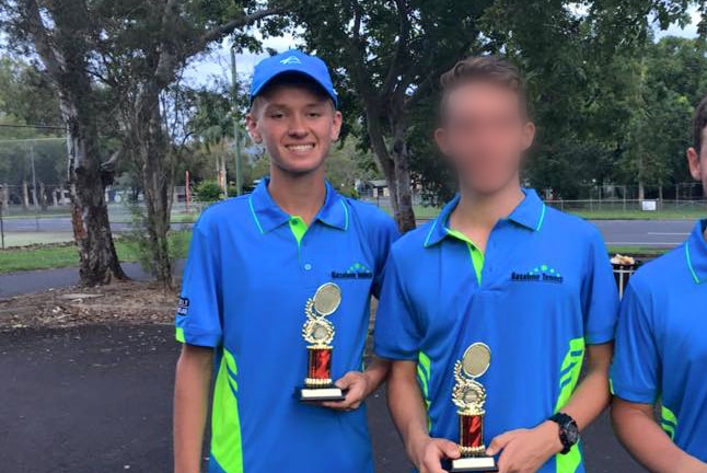 A young man in tennis gear holds a trophy and smiles.