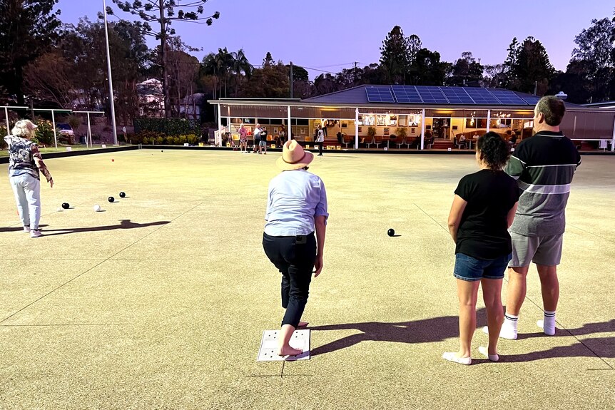 People play bowls in low light at a bowling club.