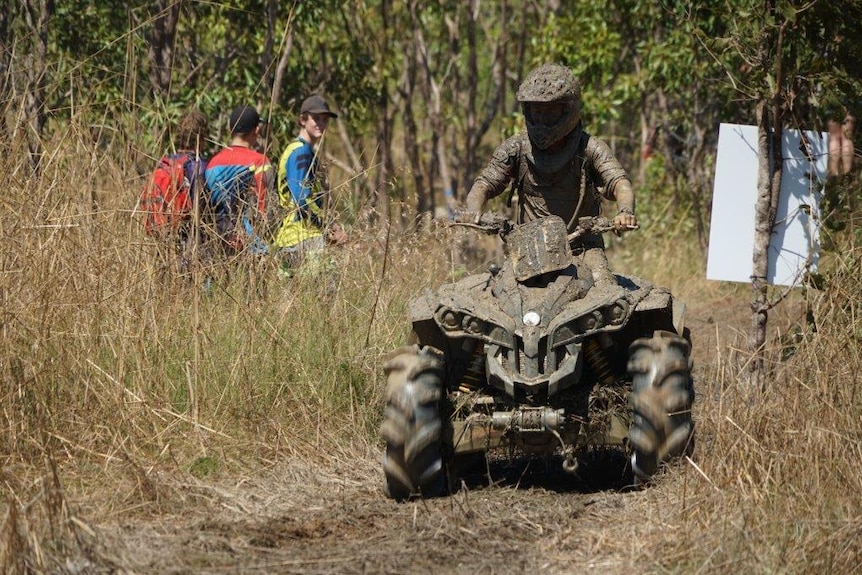 A quad bike rider caked in mud