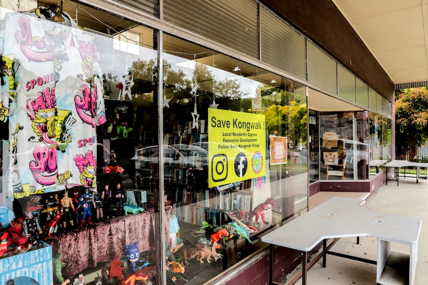 A yellow sign reading Save Kongwak displayed in the window of a second hand store with books and clothing, on a quite street