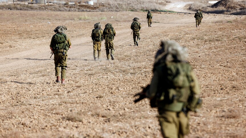 Israeli soldiers walk on grassy terrain.