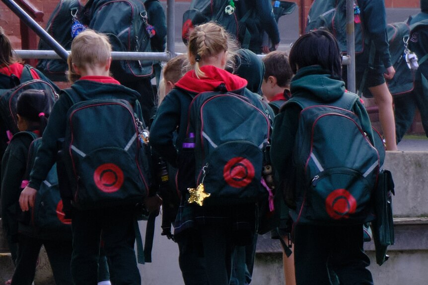 A group of early years primary school students walk into class with their backpacks on.