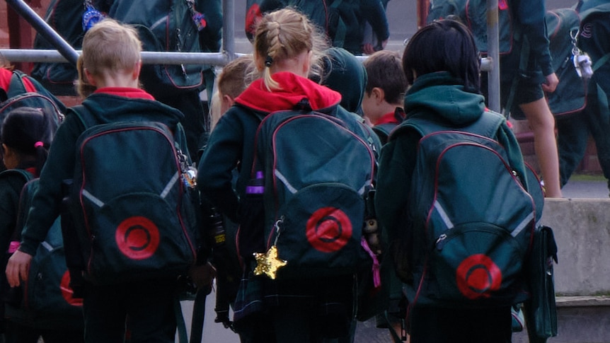 A group of early years primary school students walk into class with their backpacks on.