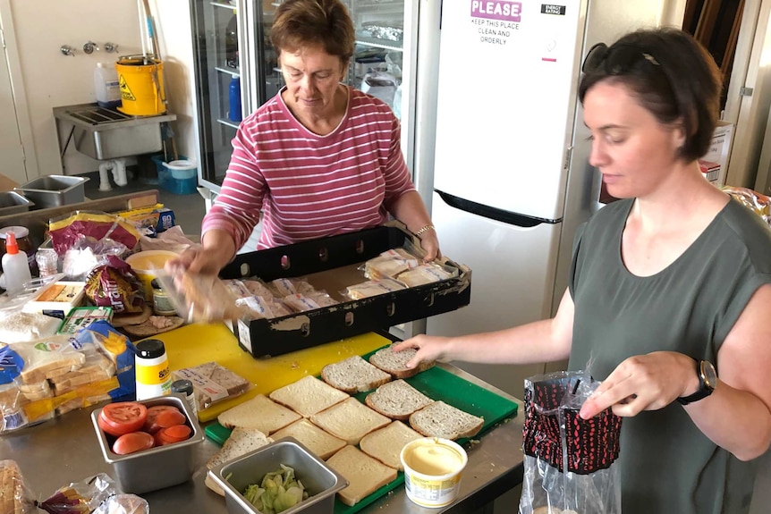 Two women prepare sandwiches in a kitchen.