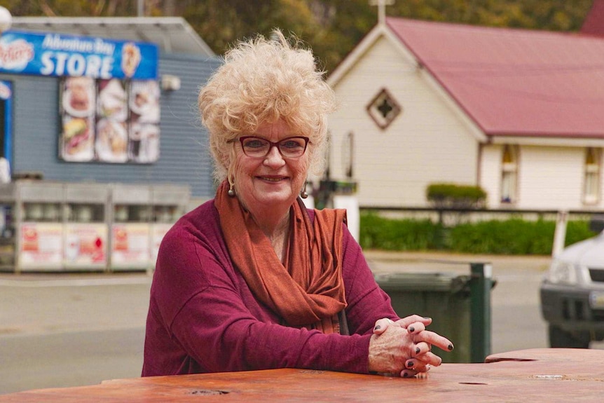 An older woman with a tousled head of grey hair sitting outside in a small town.