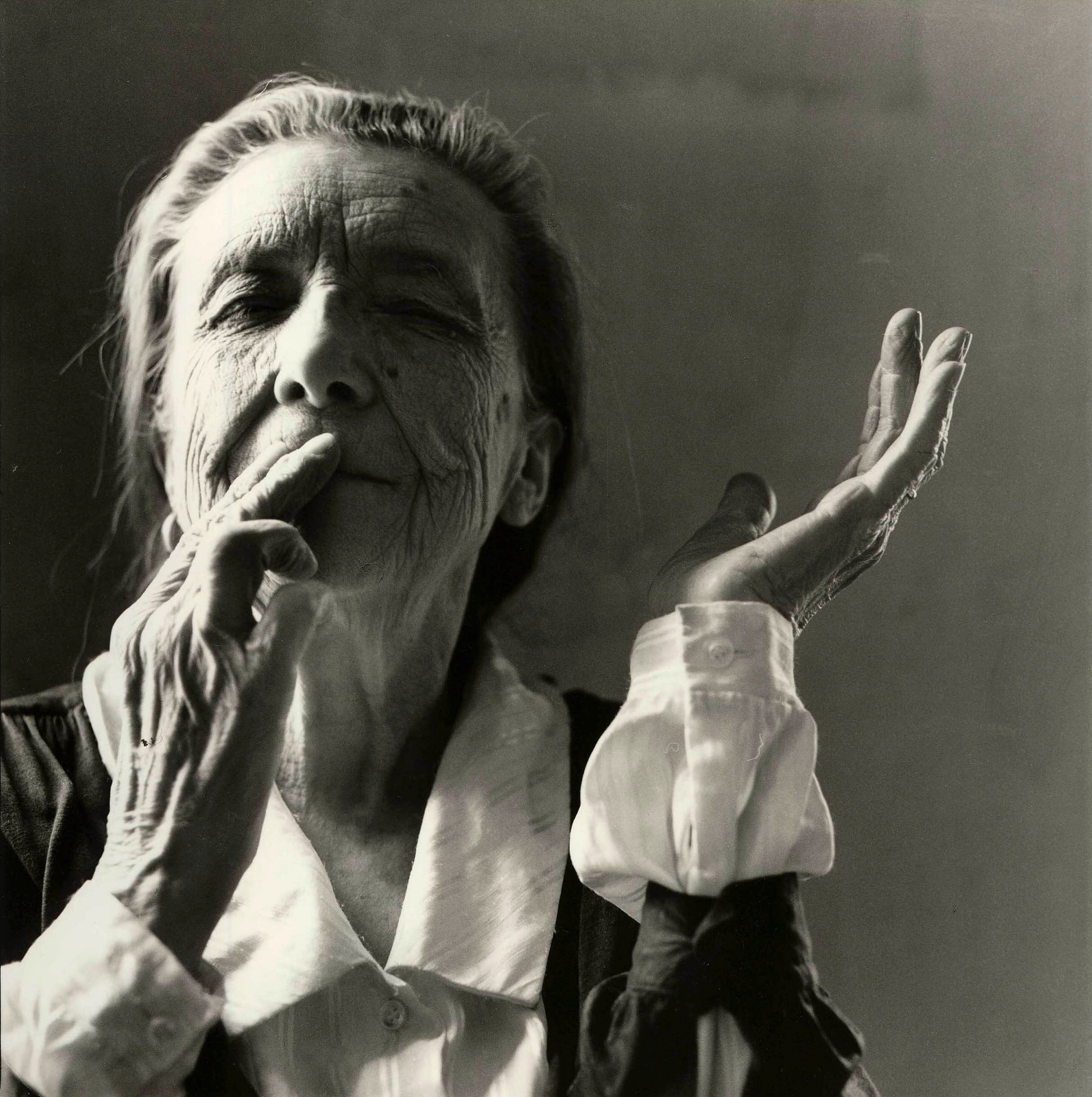 A black and white portrait of Louise Bourgeois, an elderly woman wearing a black and white blouse touching her hands to her lips