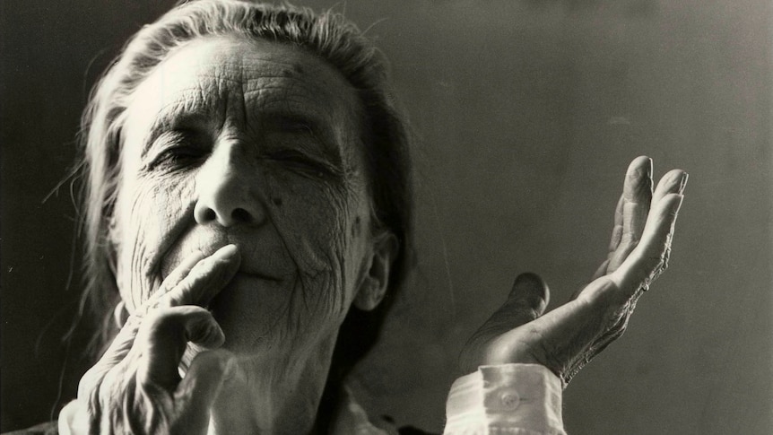 A black and white portrait of Louise Bourgeois, an elderly woman wearing a black and white blouse touching her hands to her lips