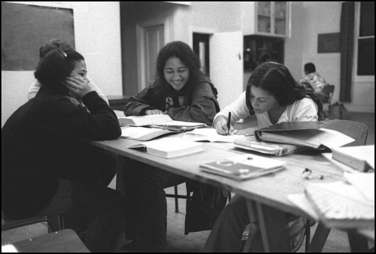 Four young women sit at a table working. 
