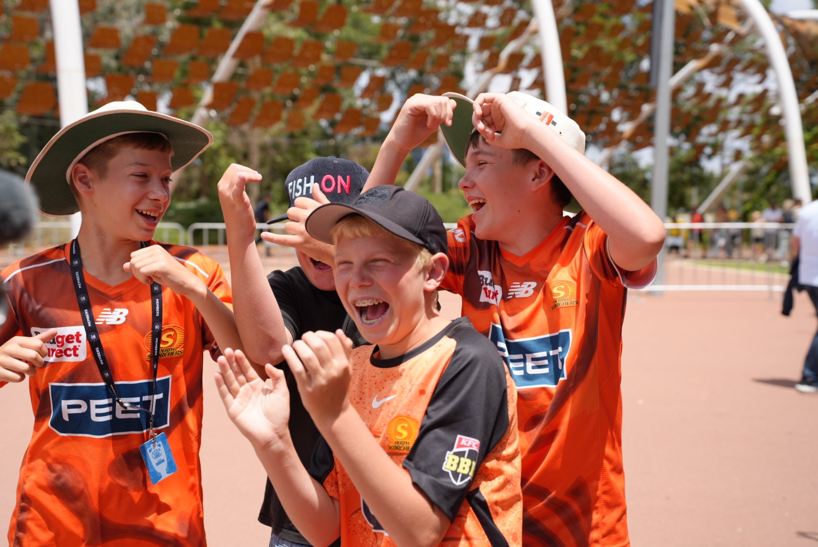 Os jovens fãs do Perth Scorchers sorriem em camisetas laranja.