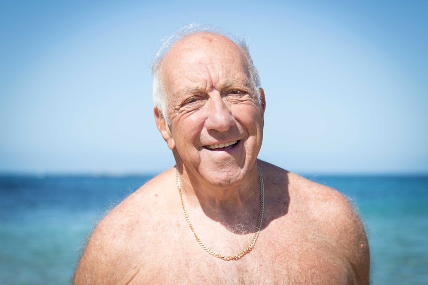 an old man standing shirtless on the beach