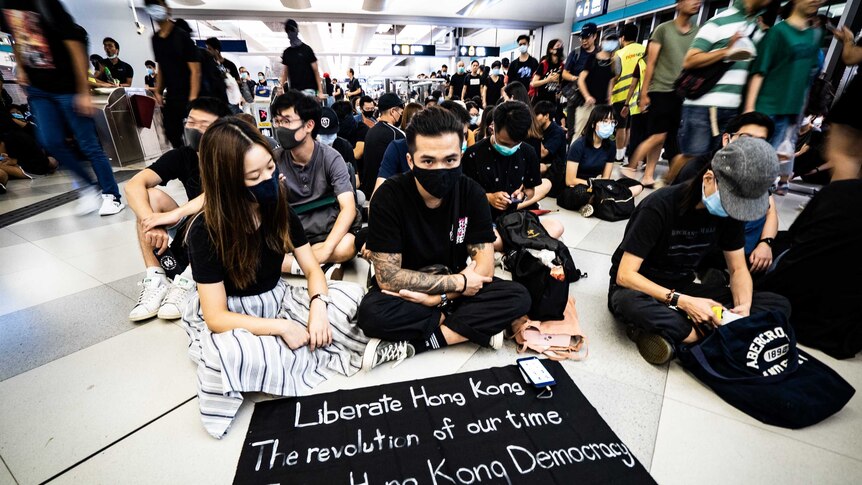 a crowd of protestors wearing black sit with signs calling for liberation.