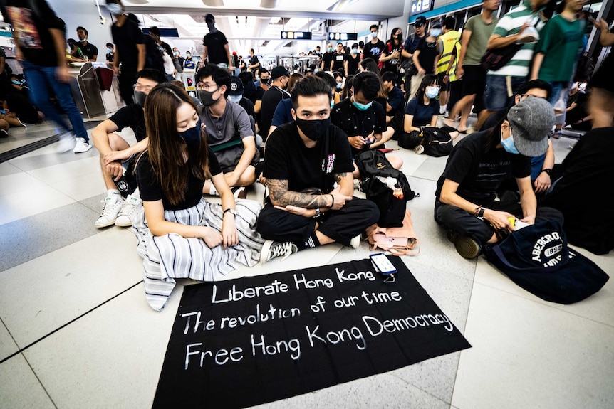 a crowd of protestors wearing black sit with signs calling for liberation.