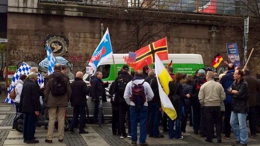 Far right Alternative for Germany supporters hold flags, turn backs at rally.