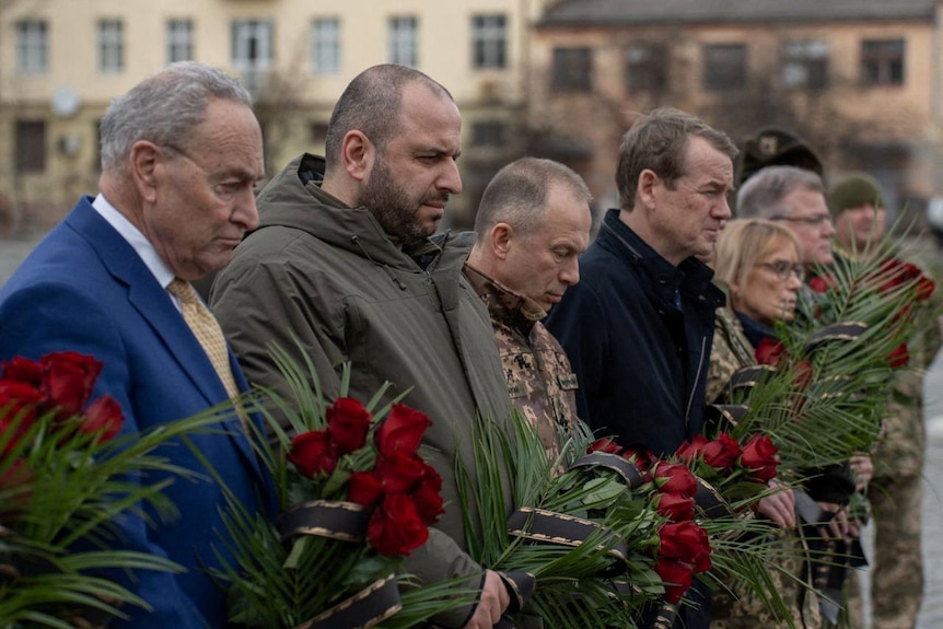 US Senator Chuck Schumer stands with Rustem Umerov and others holding flowers and bowing their heads